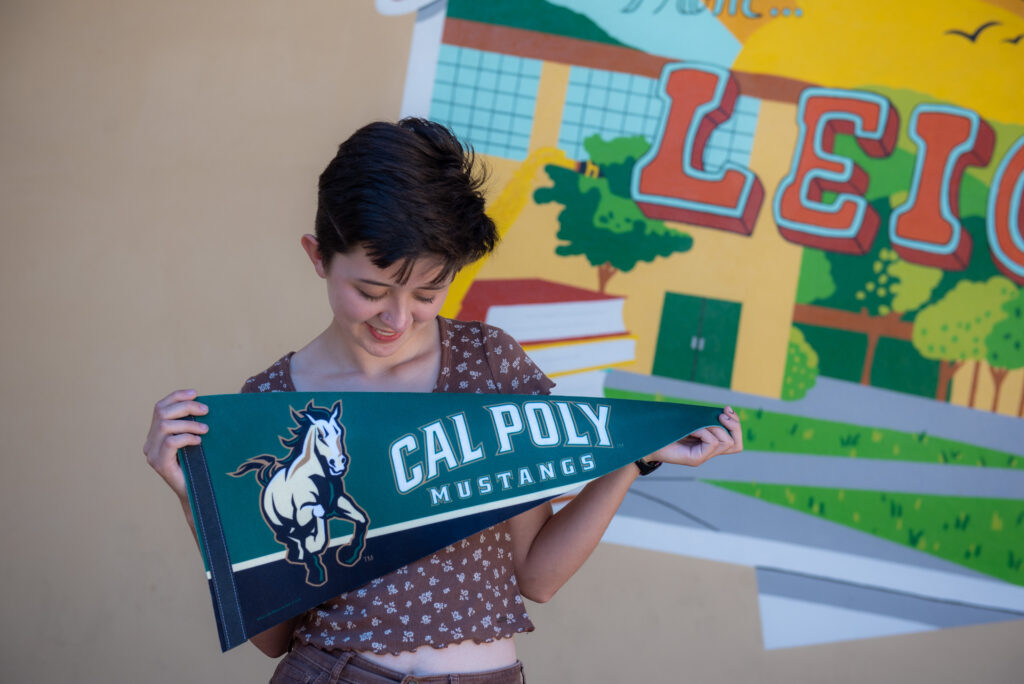Female teen girl holds green college pennant across her chest and gazes down at it.