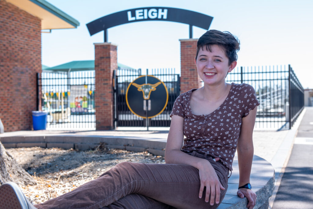 Teen female high school graduate poses in front of Leigh High school gate in California for portrait photoshoot.