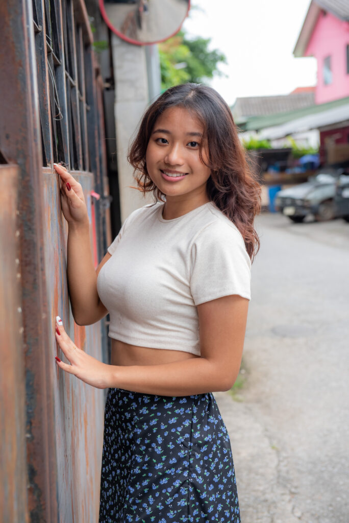 teen girl navy skirt white top leaning facing metal gate with hands on gate