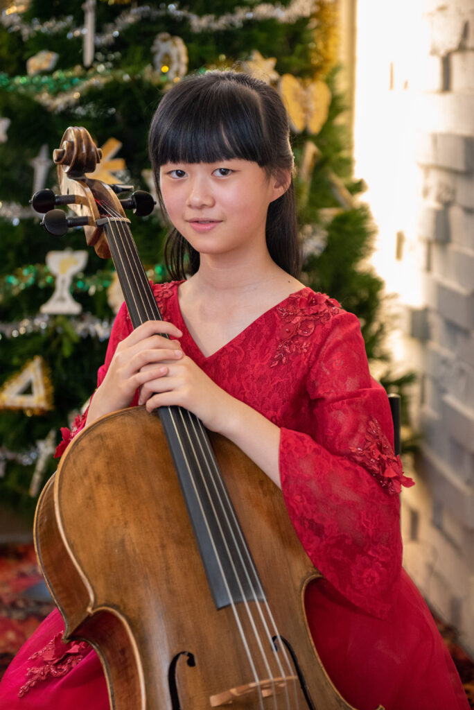 teen girl seated with cello over shoulder two hands on cello neck 