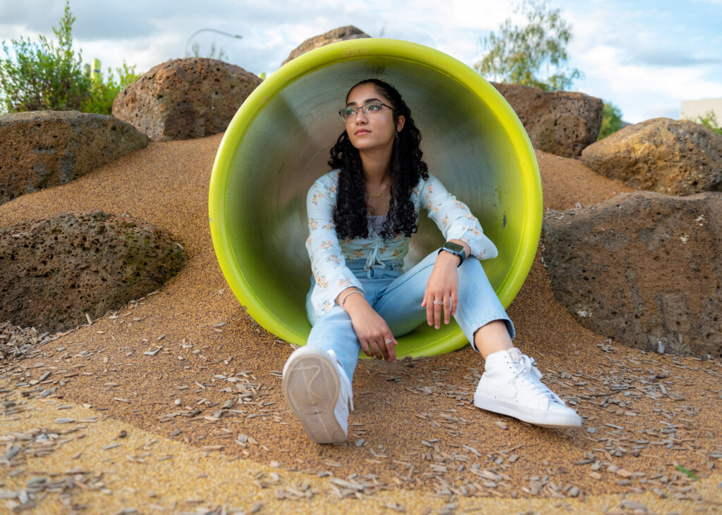 Melbourne teen girl sits inside green coloured tunnel at the playground looking into distance with one arm on her knee.