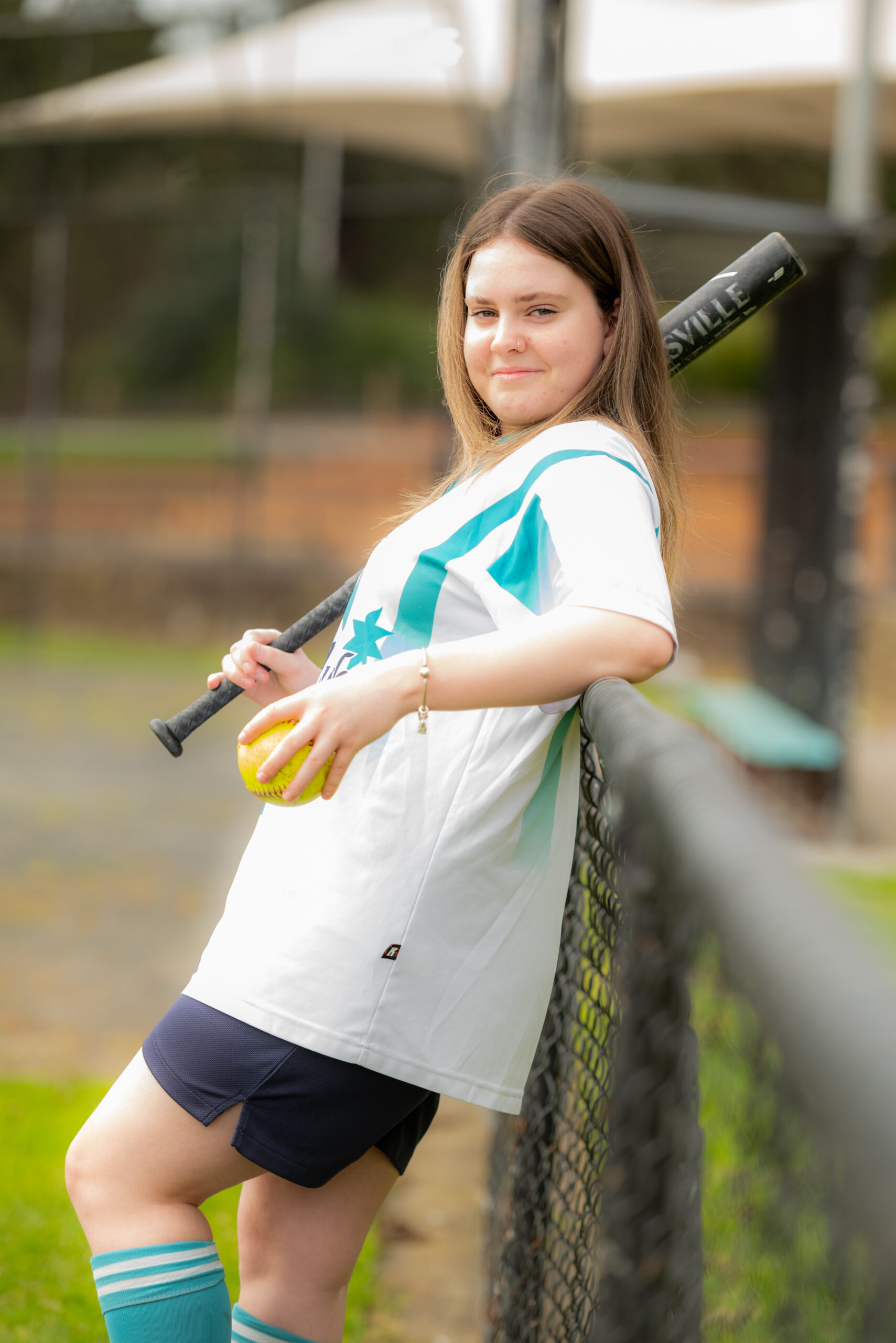 teen-girl-softball-player-leaning-fence